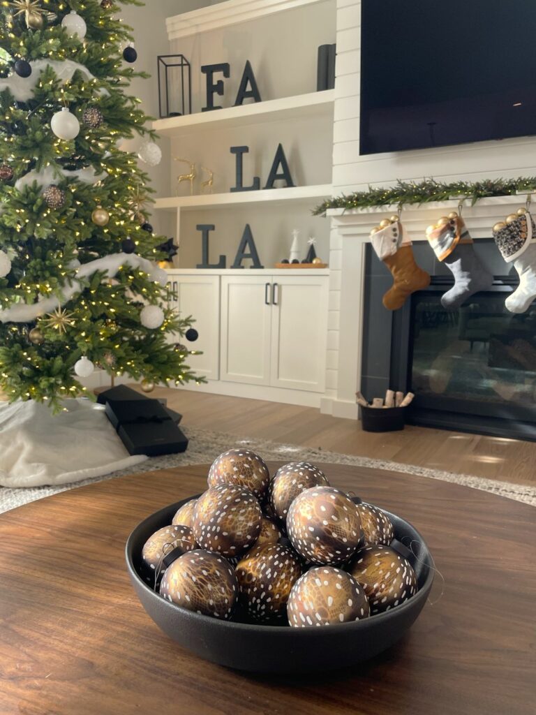 A closeup of dining room holiday décor centerpiece of three abstract silver ball ornaments sitting on rectangular matte black tray dusted in silver foiled glitter. The tray sits on a beaded silver table runner.