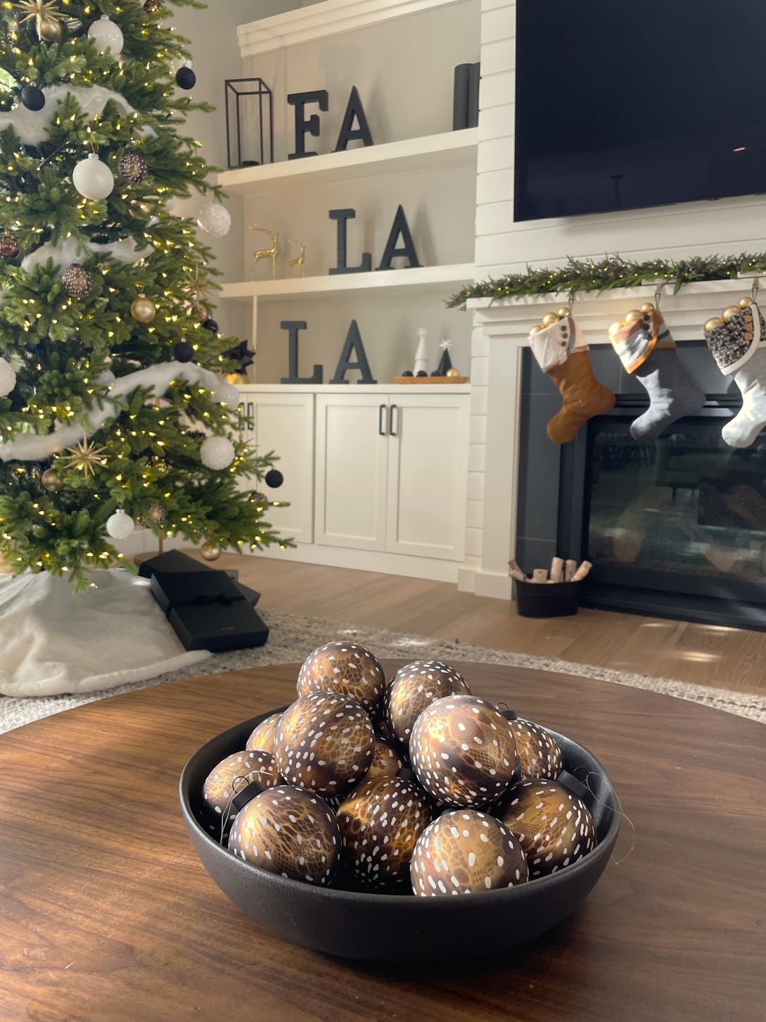 Modern Christmas decorating services in Milwaukee featuring a closeup of a dining room holiday décor centerpiece of three abstract silver ball ornaments sitting on a rectangular matte black tray dusted in silver foil glitter. The tray sits on a beaded silver table runner.