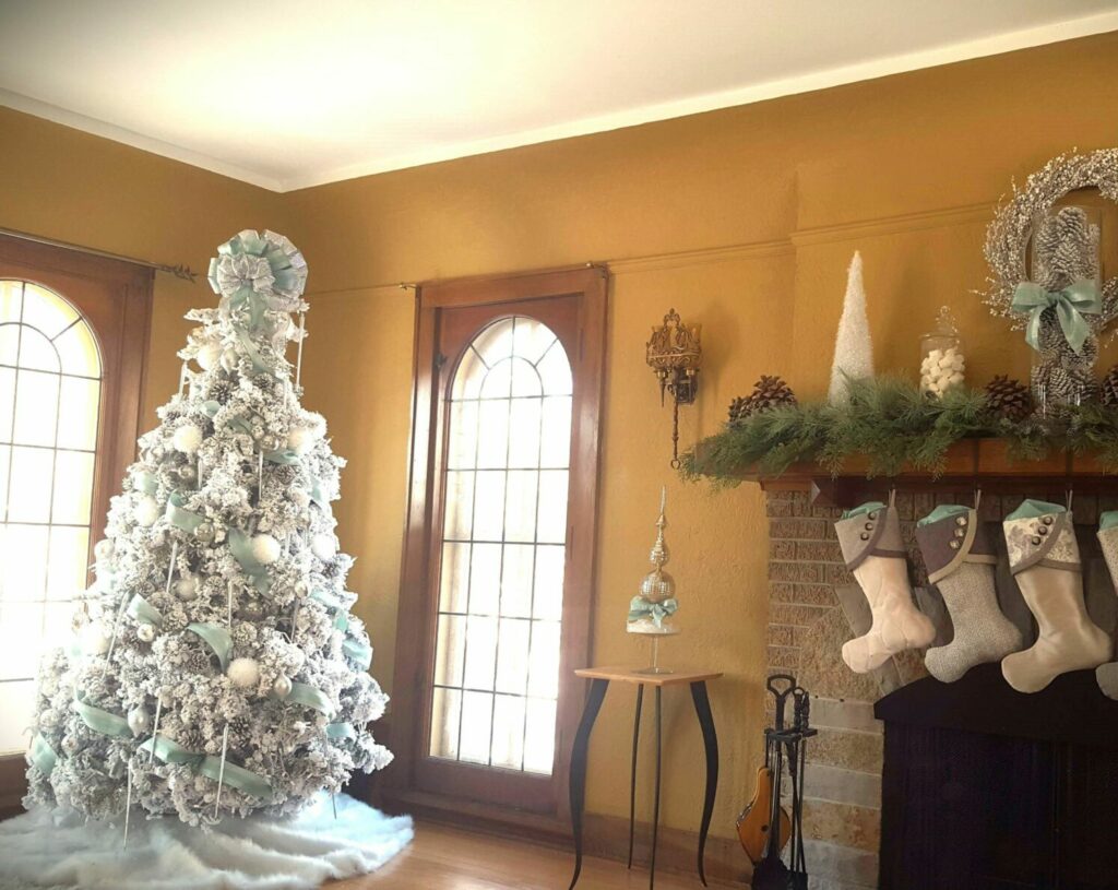 A live, white flocked Christmas tree with white, silver and aqua ornaments is the focal point of a winter wonderland holiday theme. The living room mantel is adorned with neutral-toned stockings, a white berry wreath, white cones, marshmallows in apothecary jars and greenery.