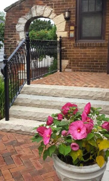 A portion of a brick walkway and brick stoop with stone steps and decorative iron railing.