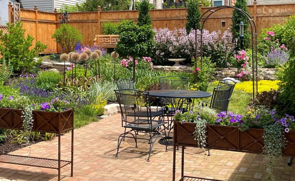 A garden design created by landscape designer, Kristyn Greenfield of Bloom! with brick patio, stone walls, cedar fencing, steel planter displays and dramatic blooming plants in Wauwatosa WI.