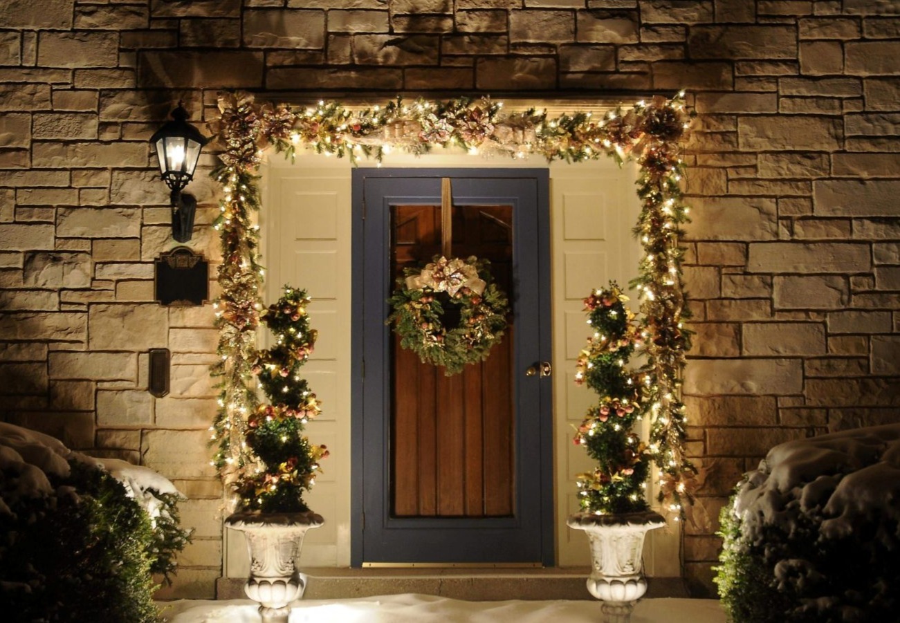 Bloom! Landscaping provides exterior holiday decorating services like this formal, custom-made garland, wreath and spiral topiaries lighted with warm, white lights and decorated in champagne gold and blush pink decor on a colonial home in Wauwatosa.