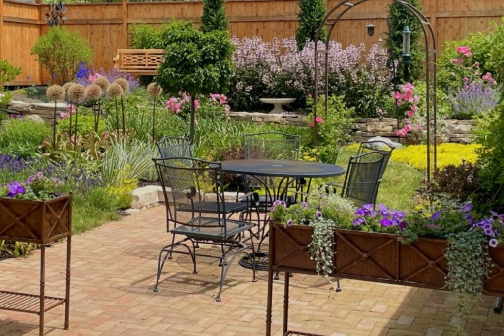 An English-inspired backyard garden is a product of Bloom! Landscaping’s Wauwatosa landscape design, installation and annuals display services. There's a charming brick patio, quant rectangular bronze planters with English cottage style annuals in purples. The gardens is filled with blooming roses, penstemon and catmint.