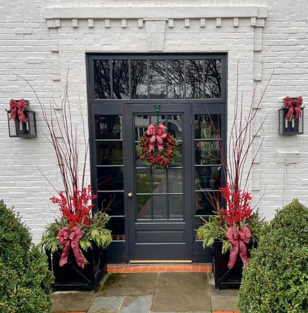 Traditional planter displays of dramatic five-foot redtwig dogwood stems with red berries, live greens and tartan bows accentuate the entrance of this Milwaukee home.