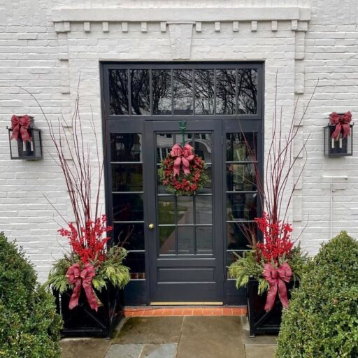 Traditional planter displays of dramatic five-foot redtwig dogwood stems with red berries, live greens and tartan bows accentuate the entrance of this Milwaukee home.